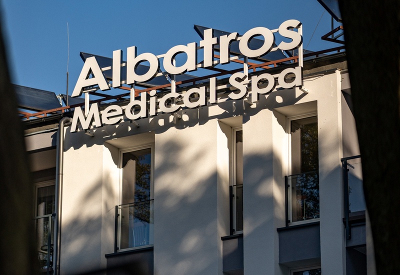 Napis 'Albatros Medical Spa' na dachu nowoczesnego, białego budynku hotelu z wąskimi balkonami i szklanymi poręczami.