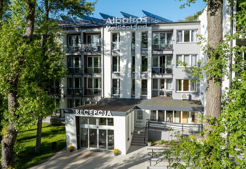 Albatros Medical Spa — nowoczesny hotel z balkonami, widoczną recepcją i panelami słonecznymi, otoczony dużymi drzewami