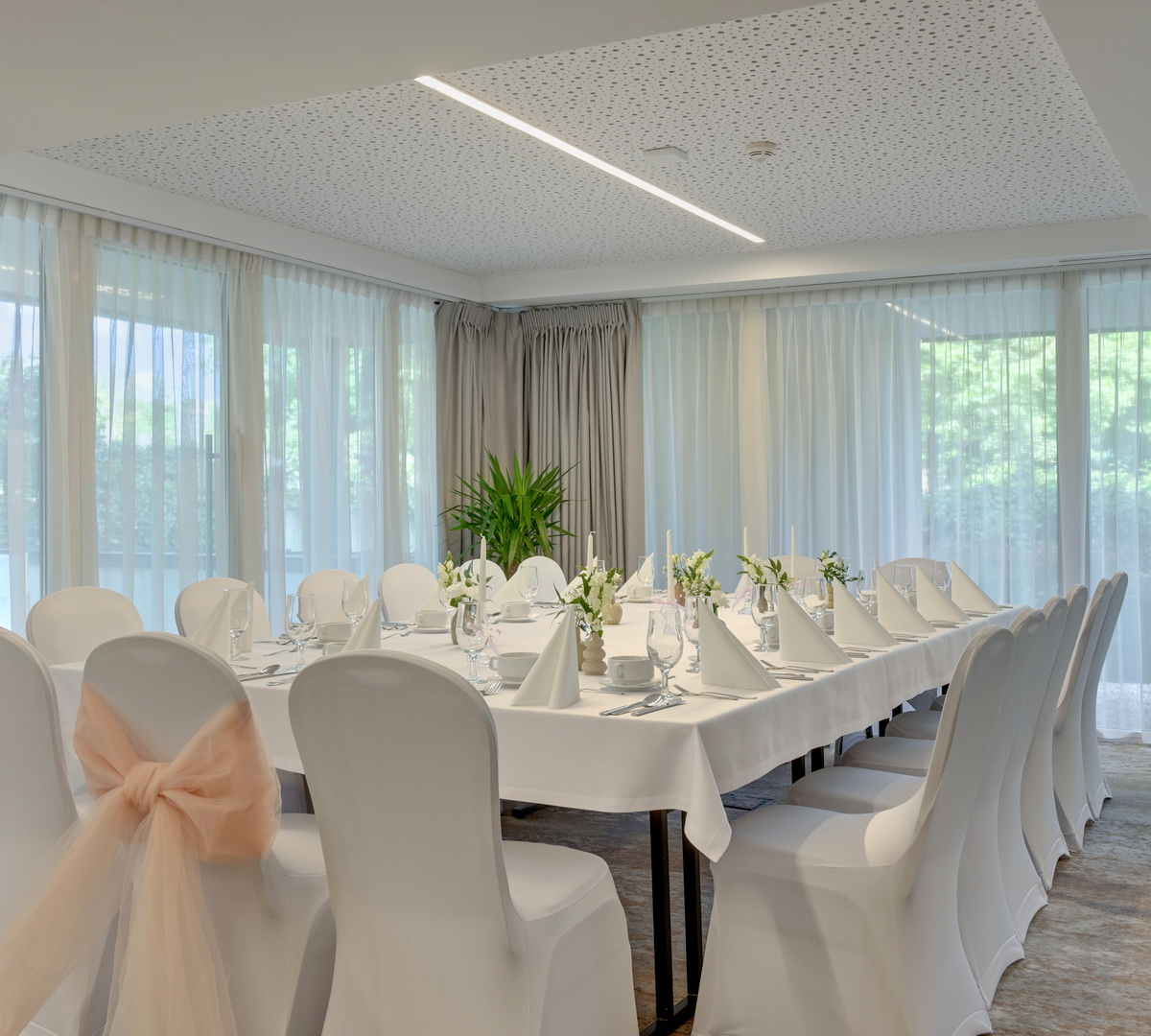 Elegant dining/banquet room with long table set for event — white linens, chair covers with peach bow, candles, florals