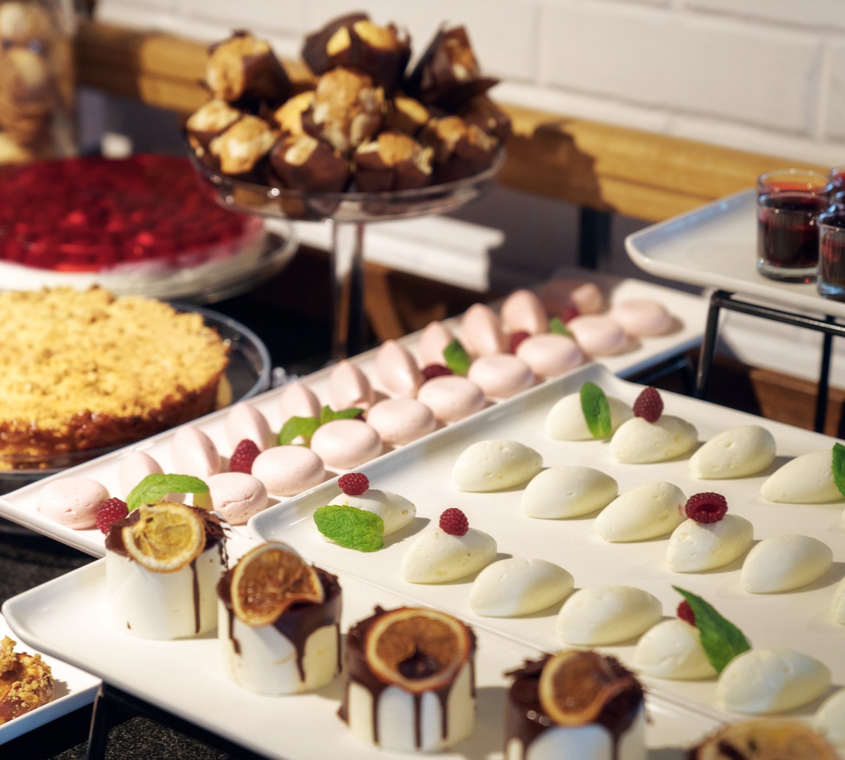Dessertbuffé med utvalg av bakverk: hvite mousse-domer med bringebær og mynte, rosa makroner, smuldrekake og små sjokoladeovertrukne kaker