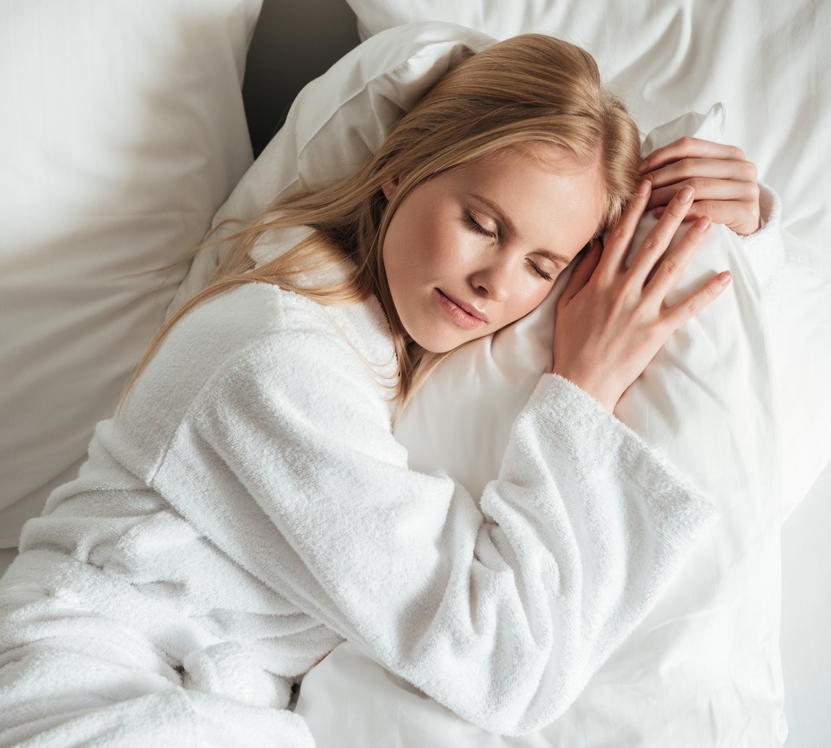 Gast schläft ruhig auf weißem, weichem Bett im Bademantel, mit frischer Bettwäsche und weichen Kissen