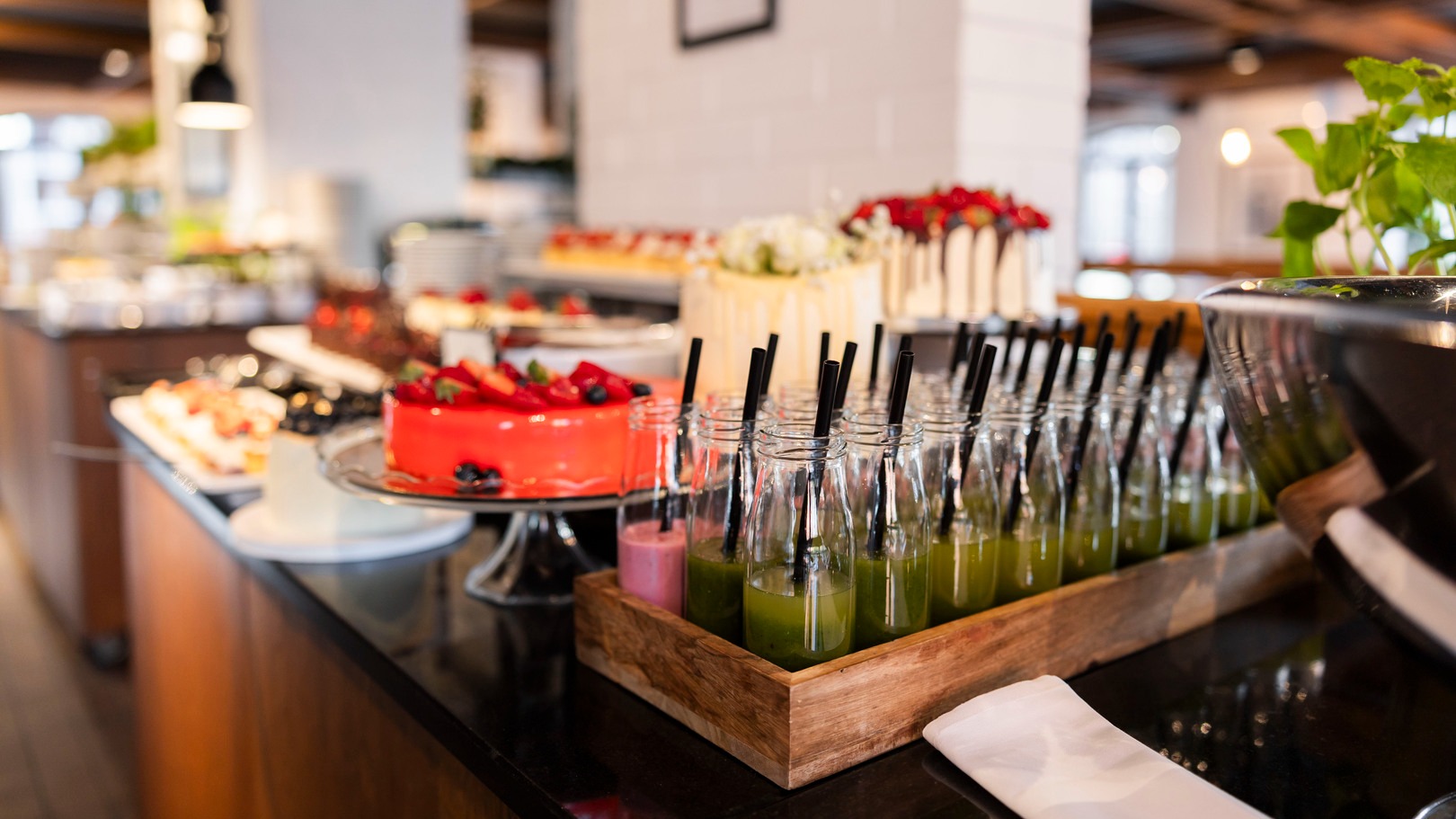 Bufet deserowy i soków z rzędami zielonych smoothie w butelkach ze słomkami, czerwoną glazurowaną tortą i wypiekami