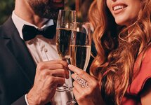 Par i formella kläder skålar med champagneglas, varmt festljus och romantisk hotellstämning.
