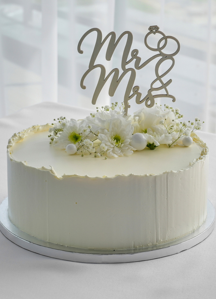 Enlaget hvit bryllupskake med 'Mr & Mrs'-topper og friske hvite blomster på et duket selskapsbord