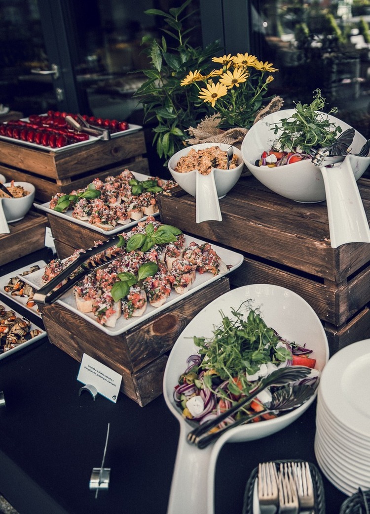 Utebuffé med friske salater og bruschetta på trekasser, stabler med tallerkener, urtepotter og gule blomster