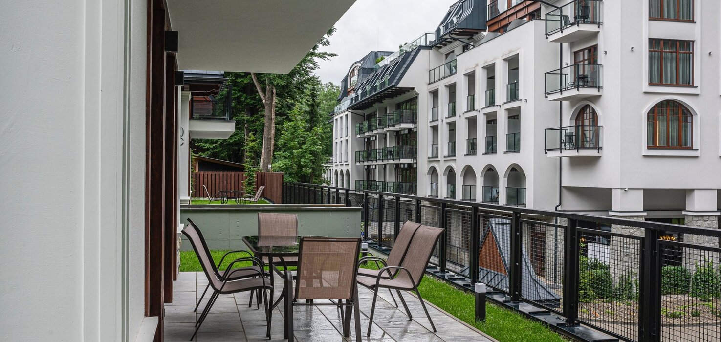 View of a small balcony with a table and chairs, and a low residential building in the background.