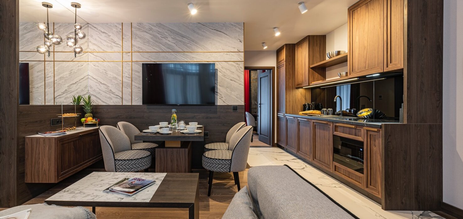 Apartament z czteroosobowym stołem z krzesłami, aneksem kuchennym, sofą i stolikiem kawowym.