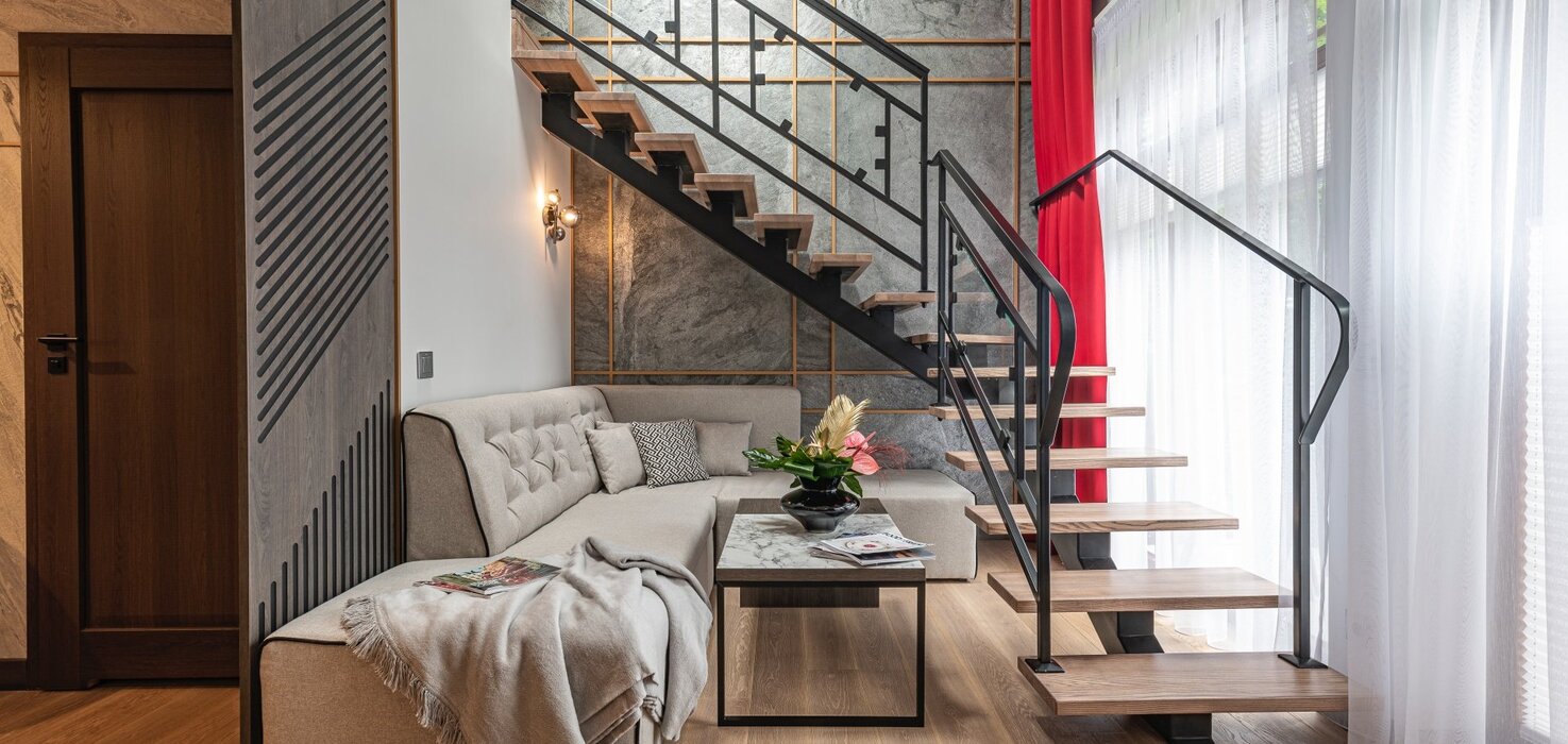 Living room with a corner sofa, coffee table and visible stairs with metal balustrade.
