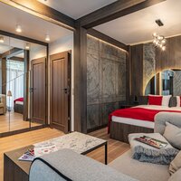 A hotel room with a bed, sofa and red curtains, part of the wall and ceiling visible.