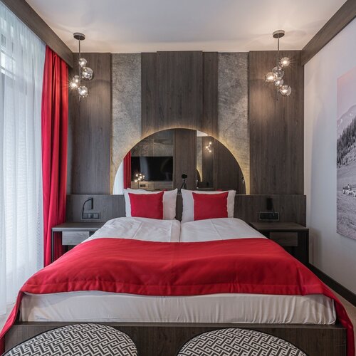 A view of a bed with a red blanket and two pouffes placed at its foot.