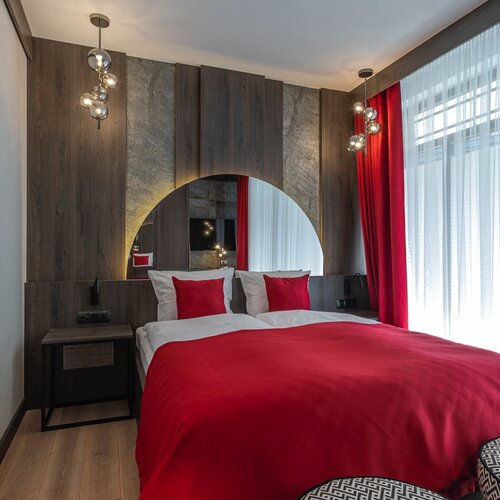Bedroom with a double bed, red bedspread and large mirror.