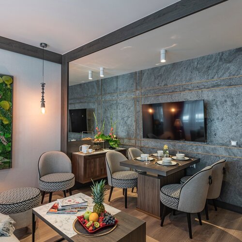 View of the living room with a sofa, coffee table, dining table and a TV on the wall.
