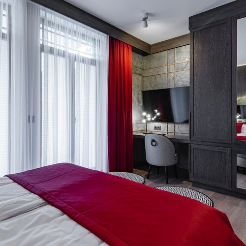 A room with a bed, a red blanket, and a desk placed against the wall with a television.