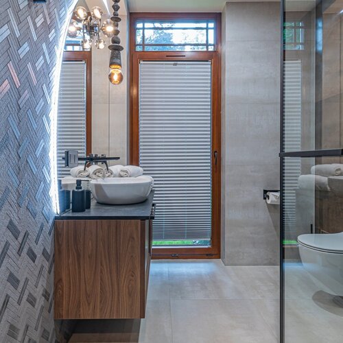 A bright bathroom with a glass shower enclosure, wooden cabinet, round washbasin and large mirror.