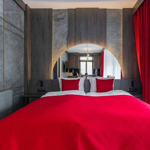 A hotel bed with a red cover positioned beneath a mirror in an illuminated frame.