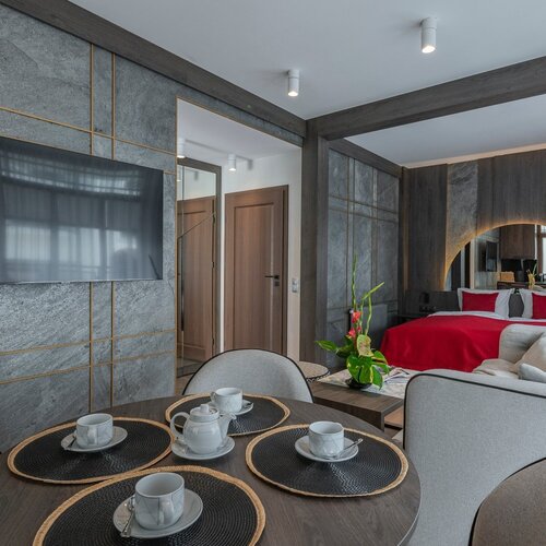 A table with coffee tableware and a view of the television, and a bed with red bedding.