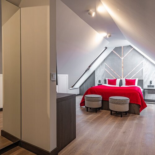 View of a double bed and two pouffes in an attic room.
