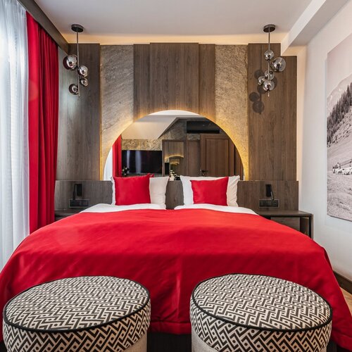 A double bed and two pouffes in front of it.