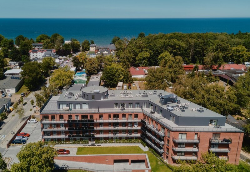 Nowoczesny hotel nad morzem z balkonami i zielonym dziedzińcem, otoczony drzewami i blisko plaży