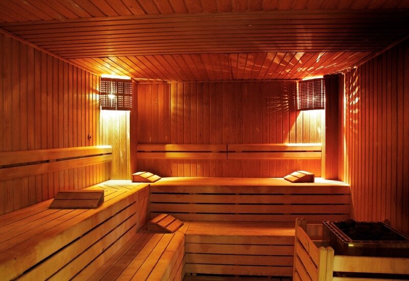 Przytulna sauna hotelowa z drewnianymi ławkami, poduszkami i ciepłym oświetleniem dla relaksu gości