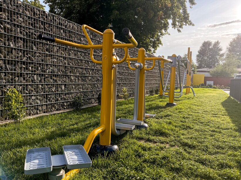 Zewnętrzne siłownie hotelowe na zielonym trawniku, wyposażone w żółte i szare urządzenia do ćwiczeń na świeżym powietrzu