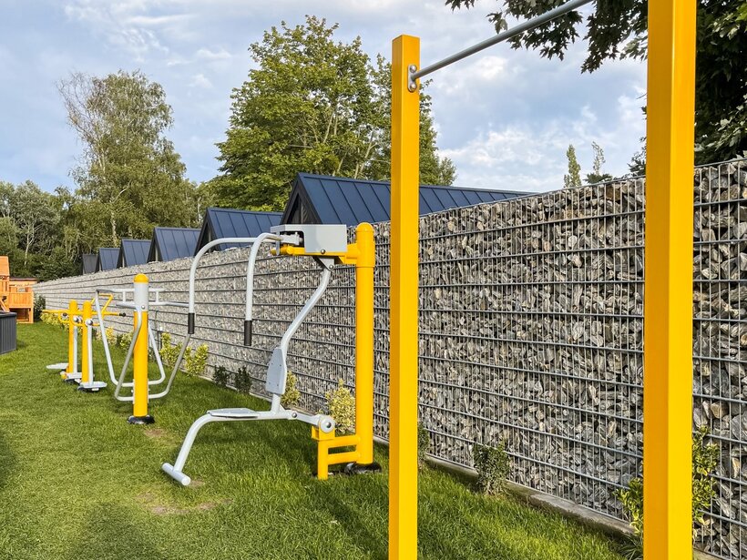 Zewnętrzne żółte siłownie na świeżym powietrzu na trawniku przy kamiennym murze w otoczeniu zieleni.