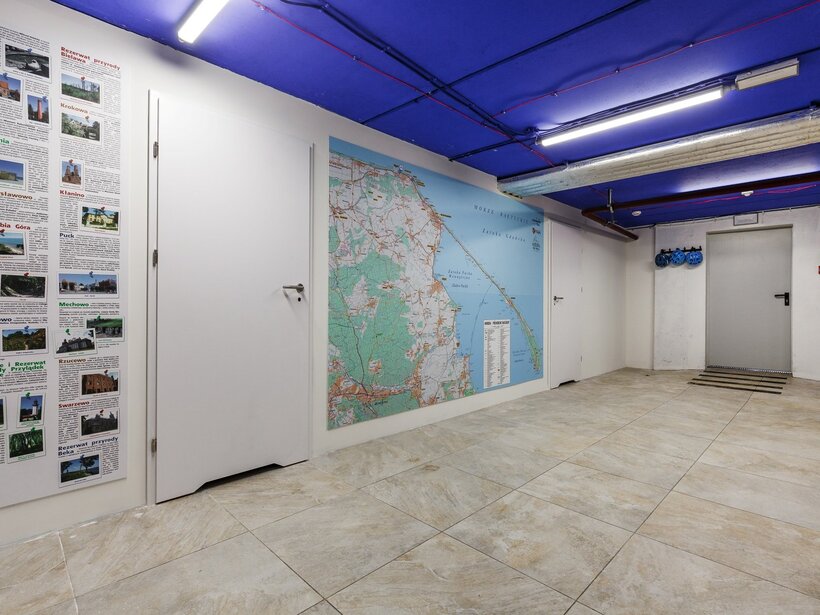 Przestrzeń hotelowa z mapą okolicy nadmorskiej i informacjami o atrakcjach, niebieski sufit i przechowywane kaski rowerowe