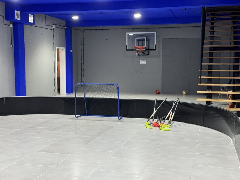 Nowoczesne, wielofunkcyjne pomieszczenie sportowe z minibramką, kijami do unihokeja i koszem do koszykówki na ścianie.