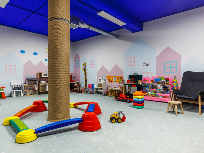 Kolorowy kącik zabaw dla dzieci w hotelu z miękkim dywanem, zabawkami i wygodnym fotelem dla opiekunów.