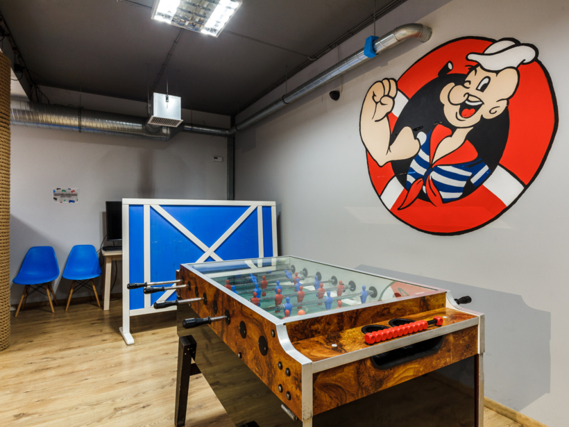 Pokój rekreacyjny z piłkarzykami, niebieskimi krzesłami i wesołym muralem marynarza na ścianie