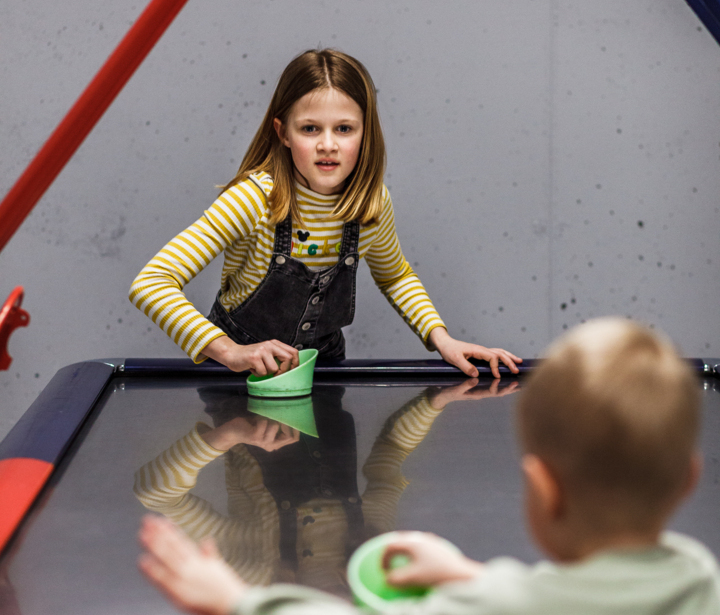 Dwoje dzieci grają w air hokeja, bawiąc się razem przy stole w hotelowej sali gier.