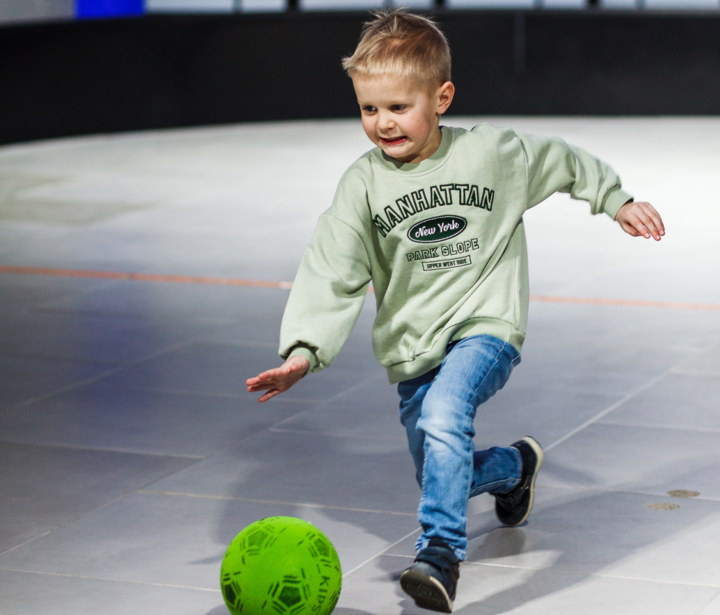 Mały chłopiec bawiący się zieloną piłką na podłodze w jasnym, nowoczesnym wnętrzu