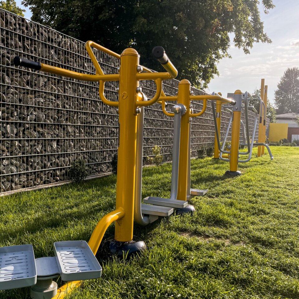 Außen-Fitnessbereich des Hotels mit gelben und grauen Trainingsgeräten auf grünem Rasen im Sonnenlicht