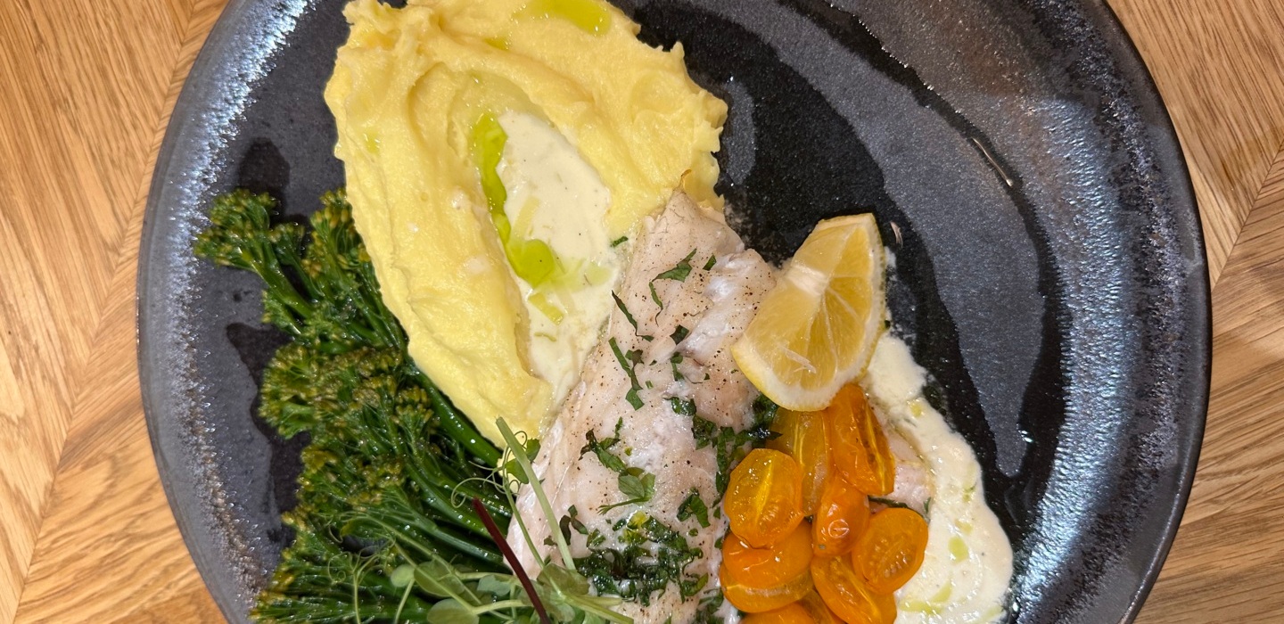 Delikatna biała ryba z sosem, pomidorki cherry, puree ziemniaczane, brokuły i plasterek cytryny na ciemnym talerzu