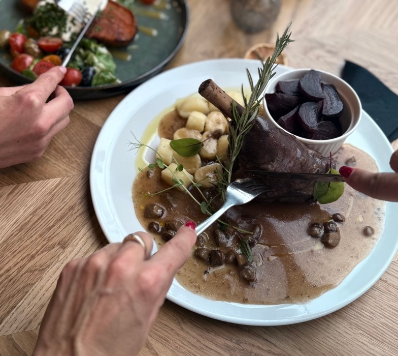 Menu hotelowej restauracji z duszoną jagnięciną, gnocchi i buraczkami, osoba kroi mięso widelcem i nożem.