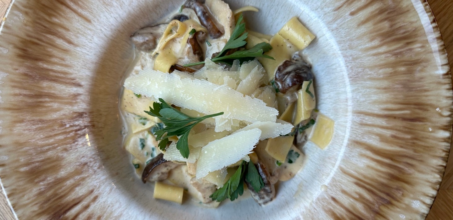 Makaron z grzybami w kremowym sosie, posypany płatkami parmezanu i świeżą pietruszką w eleganckim talerzu