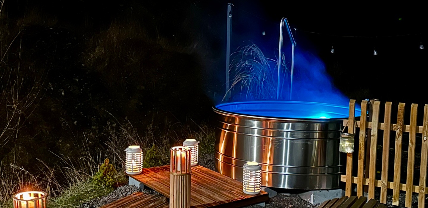 Stalowa, podświetlana na niebiesko wanna z gorącą wodą przy drewnianym pomoście i lampionach w nocnej, kameralnej atmosferze.