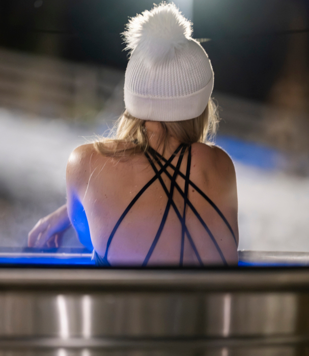 Gość relaksujący się wieczorem w podgrzewanym basenie na świeżym powietrzu, nosząca białą zimową czapkę z pomponem.
