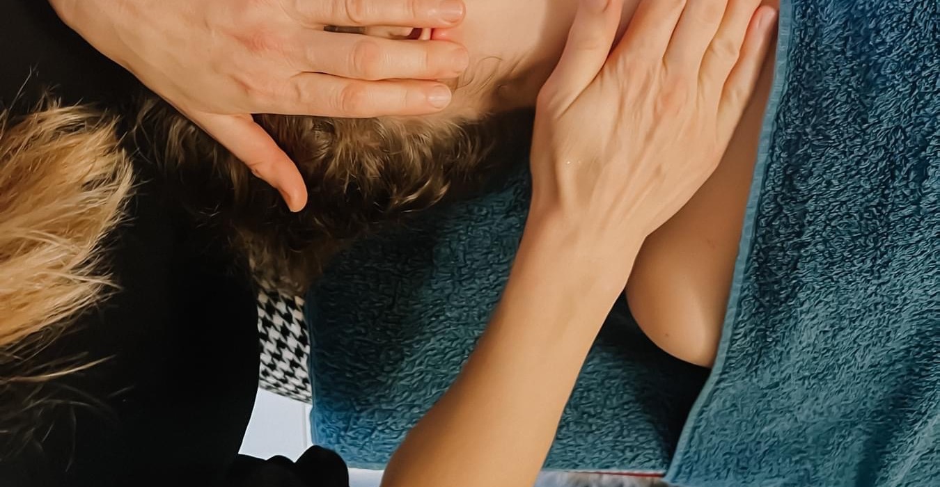 Gast erhält entspannende Kopf- und Nackenmassage auf türkisfarbenem Spa-Handtuch, Hände der Therapeutin am Gesicht.