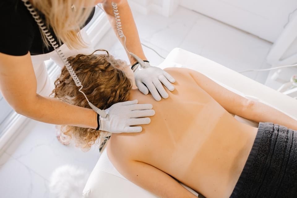 Gast erhält Schulter- und oberer Rückenbehandlung auf weißer Spa-Liege; Therapeut trägt Behandlungshandschuhe im hellen Raum.