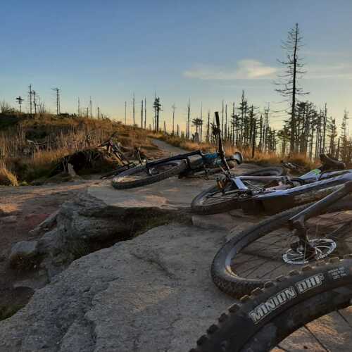 Góry o zmierzchu z rowerami górskimi leżącymi na skalistym szlaku w otoczeniu nagich drzew.