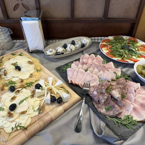 Zestaw przekąsek z wędlinami, serami z orzechami i oliwkami, sałatką z pomidorów i mozzarelli oraz kiszonymi ogórkami.