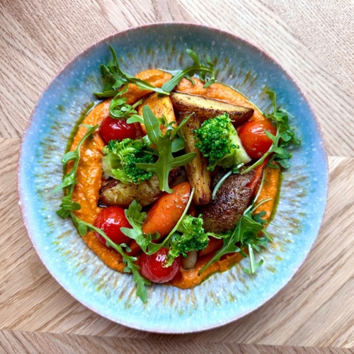 Kolorowe danie z pieczonymi warzywami, brokułami i rukolą na kremowym sosie marchewkowym na talerzu ceramicznym