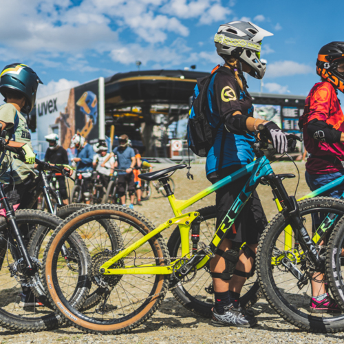 Grupa rowerzystów górskich w kaskach i ochraniaczach przygotowujących się do zjazdu w plenerze na rowerach MTB.