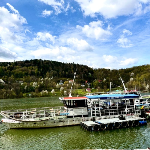 Urokliwa przystań nad jeziorem z zacumowanym statkiem pasażerskim i zielonymi wzgórzami w tle