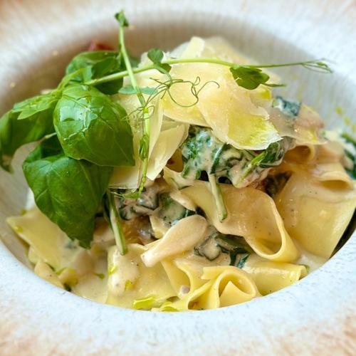 Delikatny makaron z sosem śmietanowym, szpinakiem, świeżymi ziołami i płatkami sera w eleganckim talerzu.