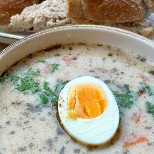 Kremowa zupa z ziołami i połówką ugotowanego na twardo jajka, podana z kawałkami chleba na białym talerzu