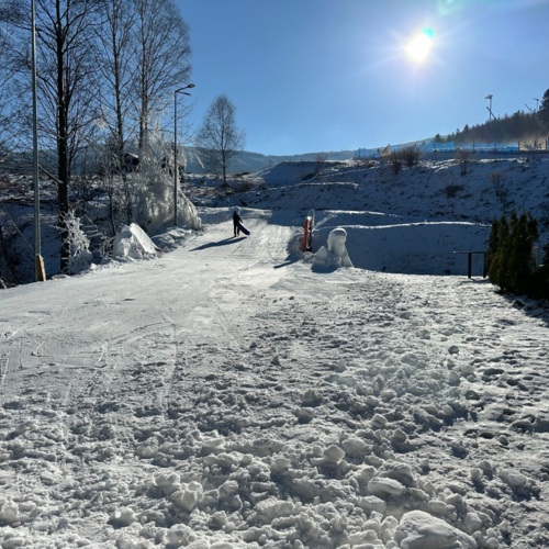 Zimowy stok z dzieckiem niosącym sankę, widok na zaśnieżone wzgórza i lasy w słoneczny dzień.