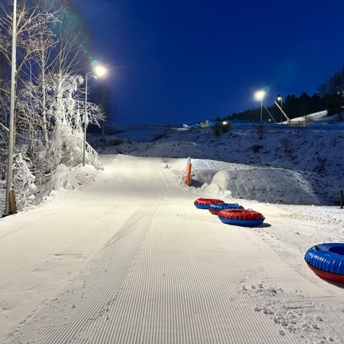 Oświetlony zimowy stok do snowtubingu z przygotowanym śniegiem i czterema czerwono-niebieskimi pontonami do zjazdów.