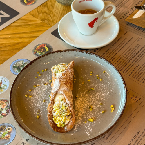 Dezert cannoli s ricottovou náplní a pistáciemi na keramickém talíři, vedle šálek espressa Julius Meinl